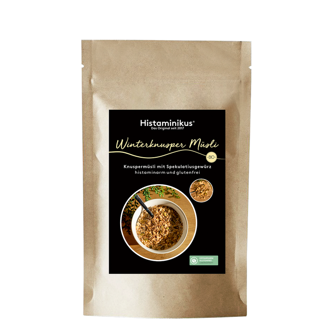 Stehende Papierverpackung „Winterknusper Müsli“ von Histaminikus  mit schwarzem Etikett, hellgelber Schrift, Abbildung einer Müslischale mit Knuspermüsli sowie Bio-Siegel und Produkthinweisen.