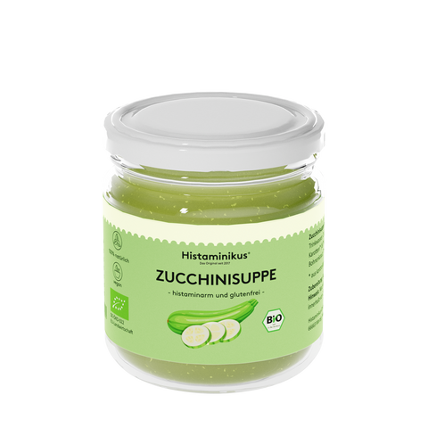 Ein Glas mit weißem Deckel, gefüllt mit hellgrüner Zucchinisuppe. Auf dem Etikett steht „Histaminikus – Das Original seit 2017“, darunter in Schwarz „ZUCCHINISUPPE – histaminarm und glutenfrei“. Abgebildet ist eine grüne Zucchini mit drei Zucchinischeiben. Symbole weisen auf 100 % natürliche Zutaten, Veganität und EU-Bio-Zertifizierung hin.